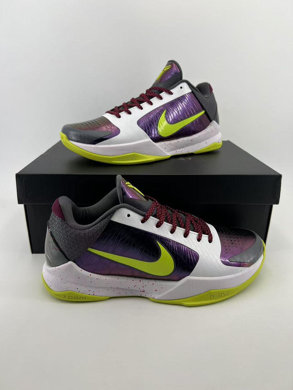 Pair of low-top Nike Kobe basketball shoes in white, iridescent purple, dark gray, and volt green.