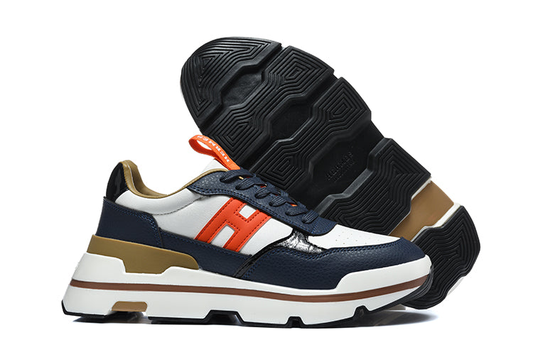 Navy, white, and orange Hermès low-top sneakers shown from the side with the black lugged outsole visible.