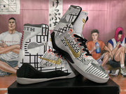 Angled view of the pair showing the patterned white upper, black laces, gold side branding, and black heel panels.