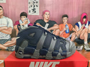 Side view of a navy and gray Nike high-top sneaker showing large AIR lettering, perforated panels, and a layered chunky sole.