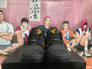 Front view of the pair showing black textured toe boxes, black laces, gold tongue logos, and a black outsole.