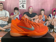 Side profile of an orange Nike Zoom basketball sneaker with textured panels, orange laces, silver Swoosh, and cushioned heel structure.
