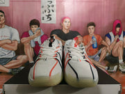 Front view of white Nike basketball sneakers with orange-red and black lace accents and translucent-looking outsoles.