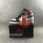 Side view of a Jordan high-top sneaker displayed on its shoe box with an orange lace set.