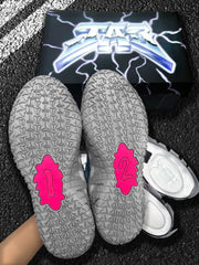 Close-up of the patterned grey outsoles with bright pink central inserts, displayed in front of the product box.