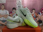 Angled view of gray-green Nike basketball shoes with contrasting Swoosh details and bright green accents