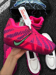 Close view of the pink and purple sneakers with side branding, patterned upper, and a product box in the background.