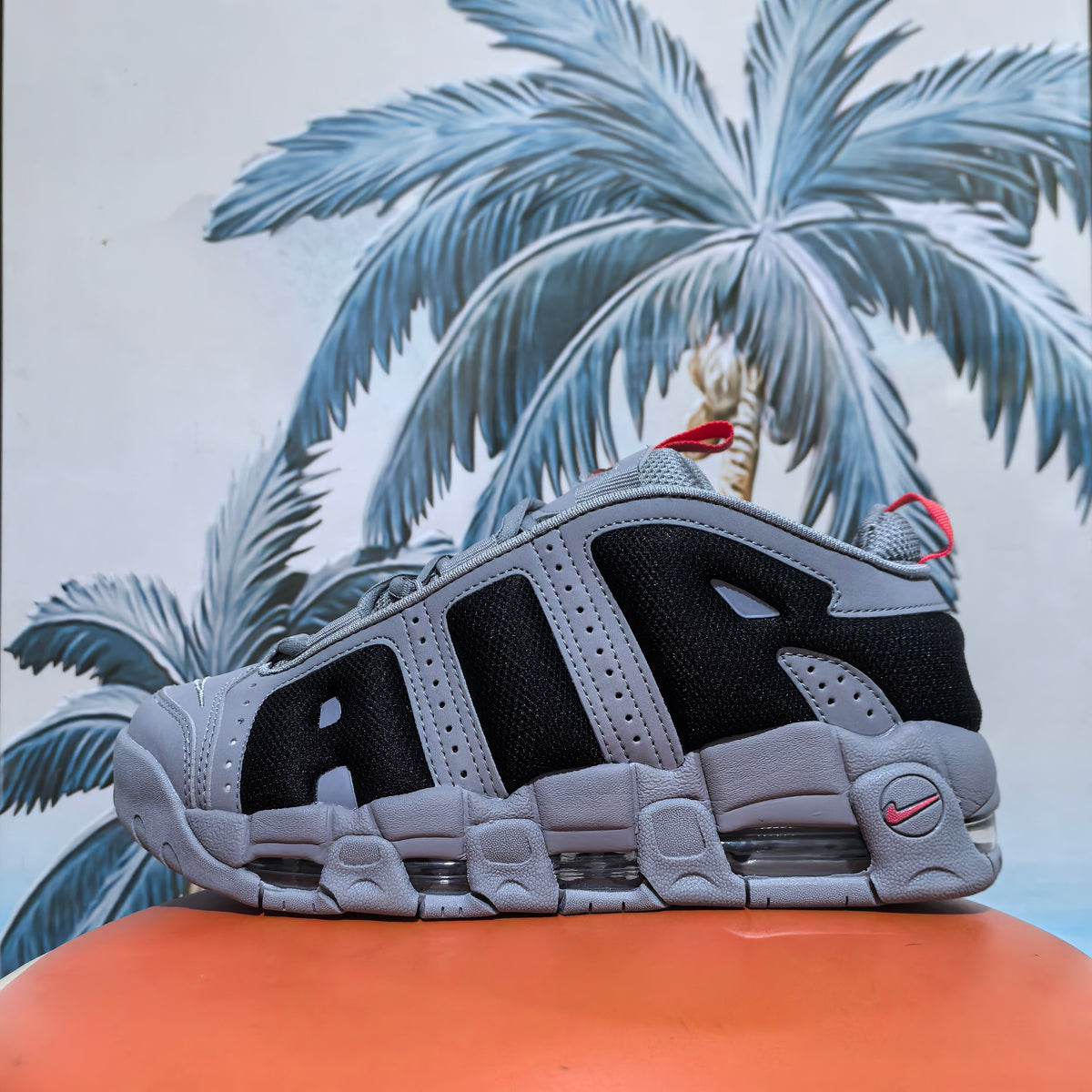 Close-up side view of gray and black Nike sneakers with layered panels, mesh sections, red pull tabs, and a segmented cushioned sole.