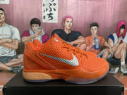 Side view of an orange Nike Zoom sneaker with textured panels, orange laces, silver Swoosh detailing, and a translucent outsole.