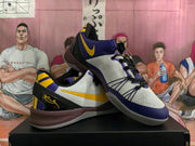 Pair of white Nike Kobe basketball shoes with purple and yellow accents, shown at an angle.