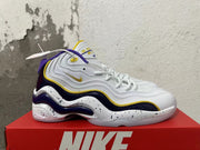 Side view of white Nike sneakers with wavy overlays, purple checkerboard panels, yellow trim, and speckled midsoles.