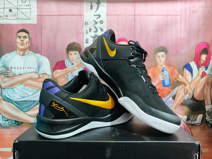 Pair of black Nike basketball sneakers with gold Swoosh branding, purple heel accents and white outsoles displayed on a box.