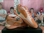 Angled view of the orange Nike sneakers showing the silver and teal Swoosh, patterned side panels, and pink laces.