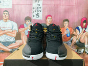 Front view of black high-top sneakers showing black laces, gold tongue details, red Jordan logos, and white toe soles.