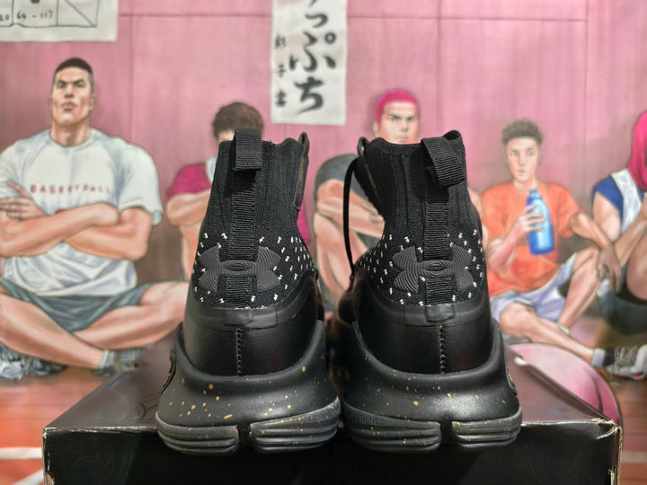 Rear view of black Under Armour basketball shoes with gold-flecked midsoles and heel pull tabs.
