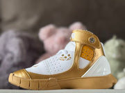 Opposite side view showing the gold strap, perforated ankle panel, white upper, and sculpted midsole.