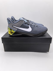 Side profile of a cool grey Nike basketball sneaker displayed on a black shoebox, showing the white side branding and translucent heel detail.