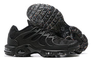Side and outsole views of black Nike Air Max Plus TN-style sneakers with small multicolor outsole details.