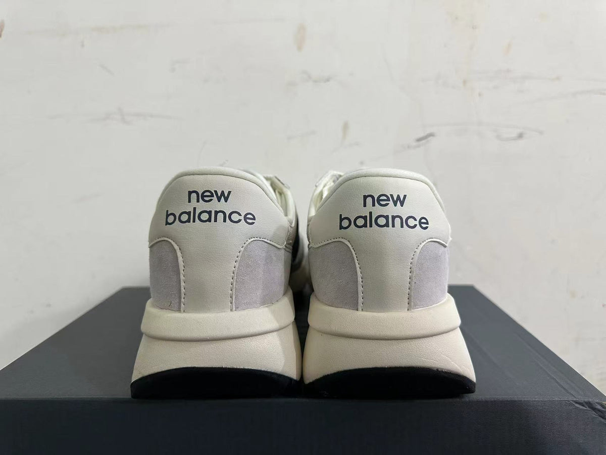 Rear view of gray and off-white New Balance U370 sneakers with navy heel branding.