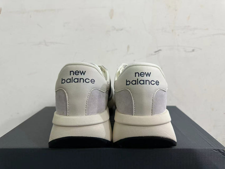 Rear view of gray and off-white New Balance U370 sneakers with navy heel branding.