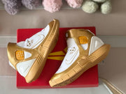 Gold and white shoes arranged on a red shoebox, with the outsole pattern visible on one shoe.