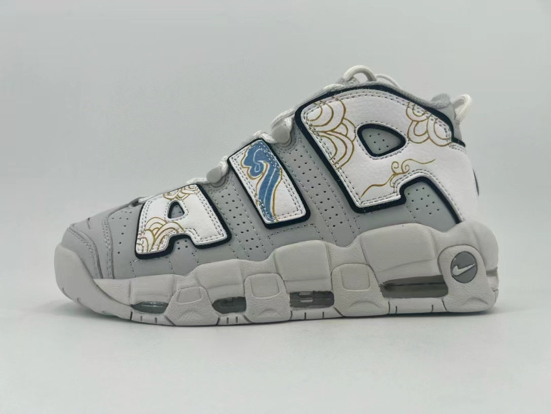 Side view of gray and white Nike Air More Uptempo sneakers with oversized AIR lettering, gold-toned decoration, and blue accents.