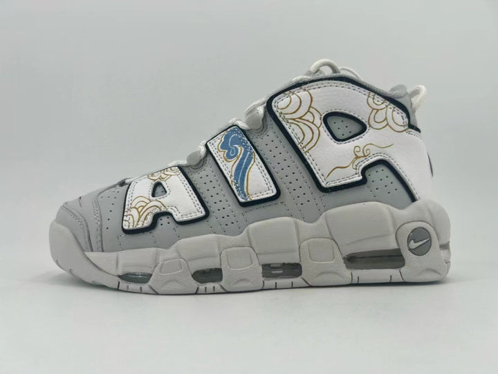Side view of gray and white Nike Air More Uptempo sneakers with oversized AIR lettering, gold-toned decoration, and blue accents.
