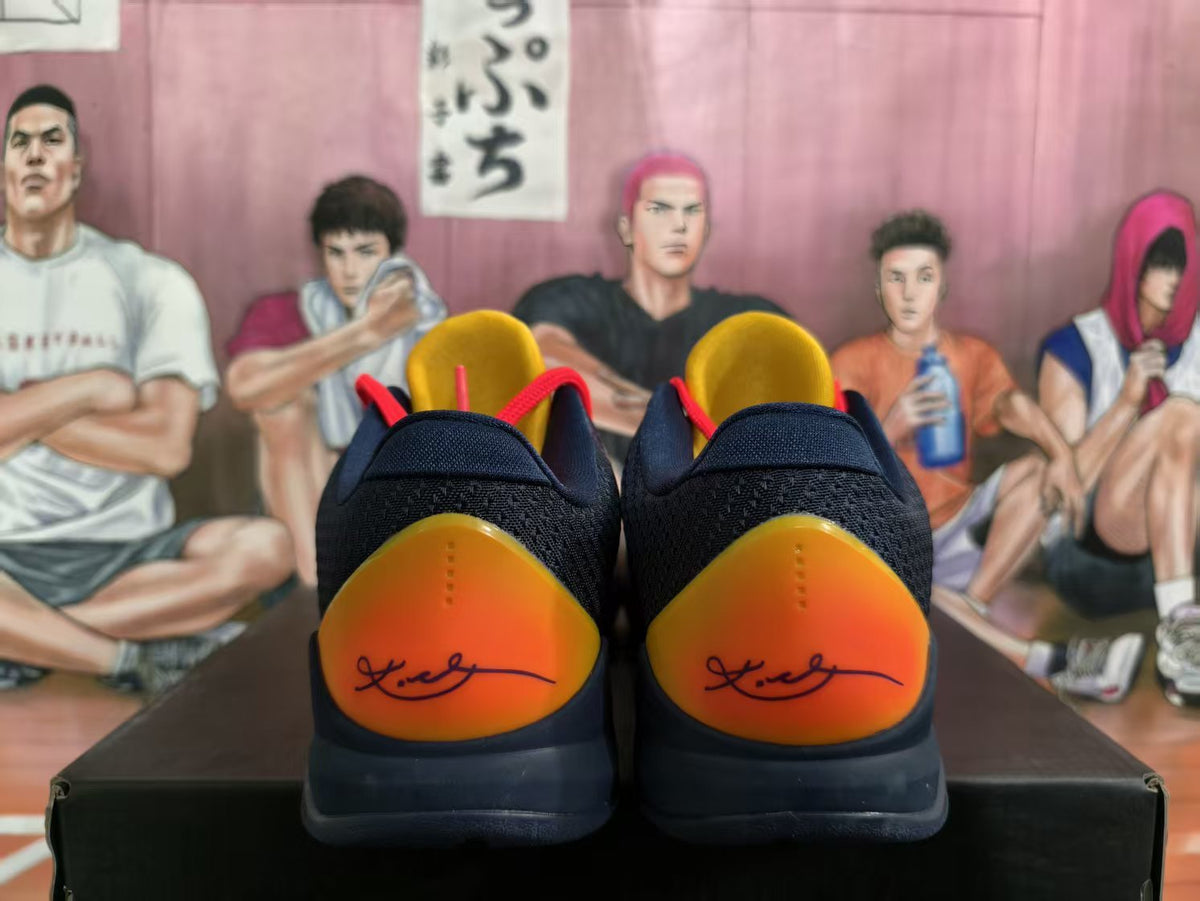 Rear view of navy Nike Kobe basketball shoes with orange-yellow heel panels and signature-style graphics.