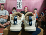 Rear view of cream ASICS basketball sneakers with tan-colored padded collars and navy heel tabs.