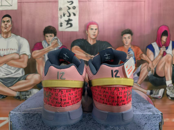 Rear view of pink Nike sneakers showing dark gray collars, red patterned heel panels, yellow-green heel accents, and the number 12.