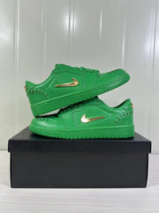Two green low-top sneakers stacked on a black shoe box, showing their side profiles and gold Swoosh details.