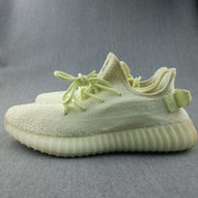Side view of pale butter-yellow Yeezy 350 V2 sneakers with matching laces, textured upper, rear pull tab, and ribbed sole.