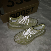 Lifestyle photo of olive green sneakers with reflective-looking laces beside a box visibly marked BOOST.