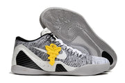 White and black low-top shoe with a yellow hanging accent and patterned outsole.