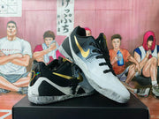 Angled view showing the black and white sneaker upper, gold Swoosh branding, black laces, and textured outsole.
