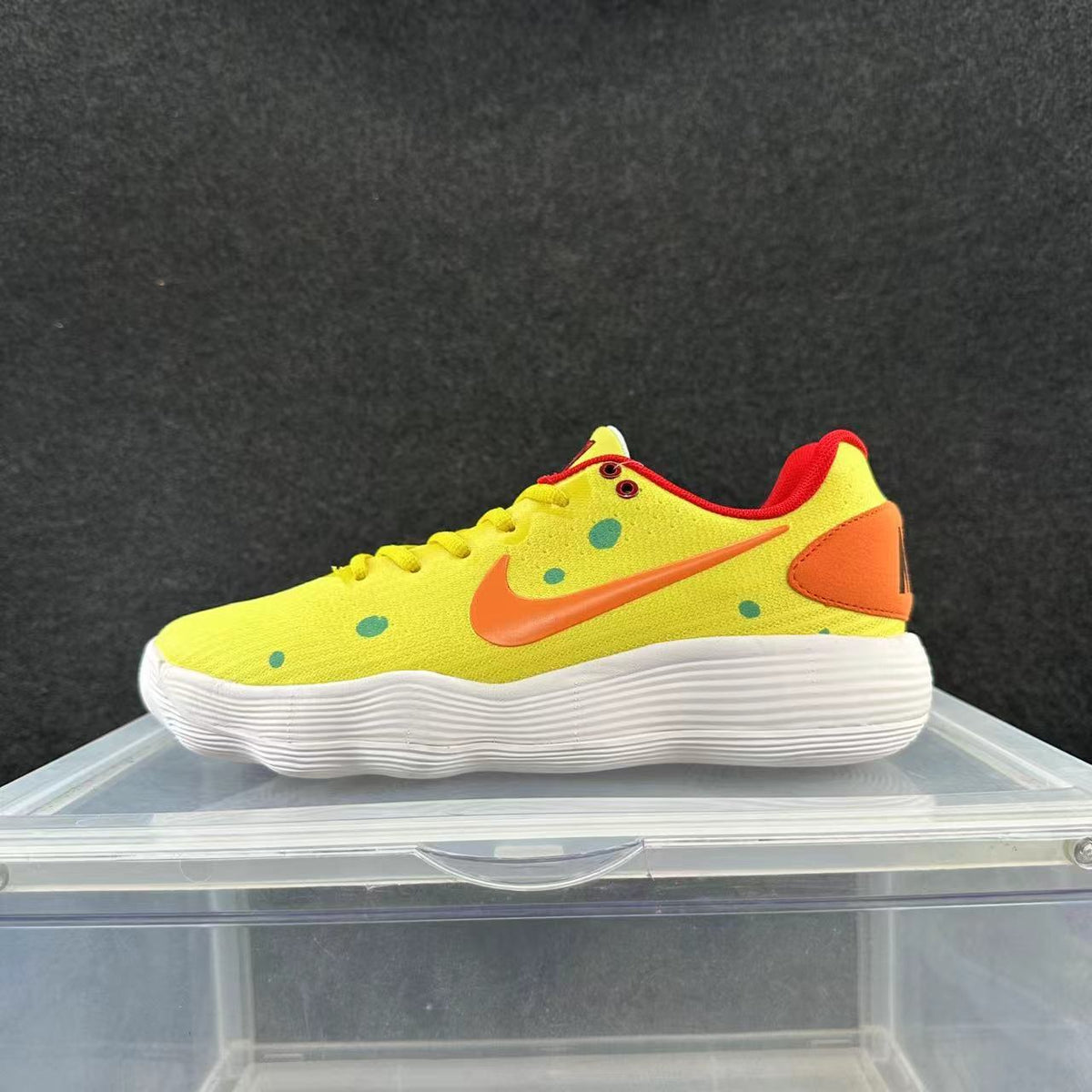 Side view of a yellow Nike low-top sneaker with an orange Swoosh and heel panel, green dots, red trim, and a white ridged-looking sole.