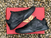 Side profile of the black sneakers displayed on a red box, with textured tonal panels visible.