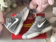 Two gray sneakers displayed on a red box, showing their side panels, high-top collars and light-colored soles.
