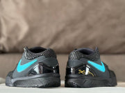 Rear view of the pair showing textured collars, glossy black heel sections, turquoise heel branding, and gold signature-style graphics.