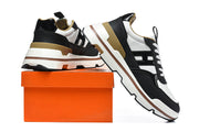 Black and white low-top sneakers with tan accents displayed beside an orange shoe box.