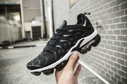 Black and white Nike TN-10 sneaker held outdoors against a brick wall.
