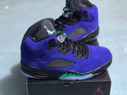 Side and three-quarter view of the purple high-top sneakers with black laces, mesh panels, and a Jordan-branded box in the background.