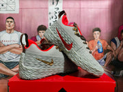 Side and outsole view of dark gray Nike basketball sneakers showing red swoosh accents, black-and-gold laces and textured detailing.