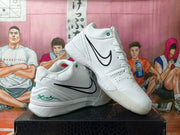 White Nike Kobe basketball shoes shown from the side, with black Swooshes and green accents.