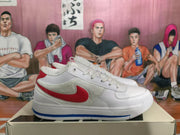 Side profile of a white Nike sneaker with a red Swoosh-style side mark, textured side panel, and blue outsole detail.