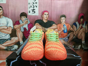 Front view of the paired orange-red Nike sneakers showing the patterned toe boxes and green laces.