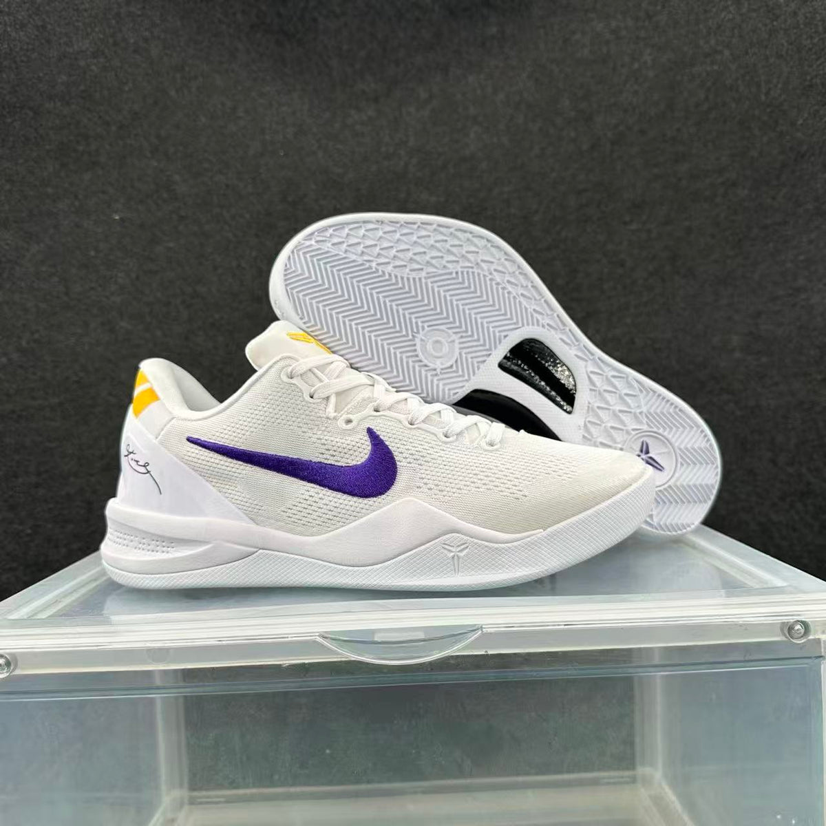 White basketball sneakers with purple Swoosh detailing and yellow heel accents, shown from the side with the outsole of the second shoe visible.