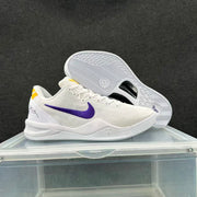 White basketball sneakers with purple Swoosh detailing and yellow heel accents, shown from the side with the outsole of the second shoe visible.