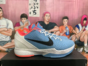 Side profile of a blue Nike Zoom basketball sneaker with a black Swoosh, white heel, speckled midsole, and orange outsole detail.
