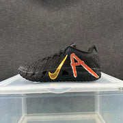 Side view of black basketball shoe showing textured upper, red-orange graphic, and gold-colored Swoosh